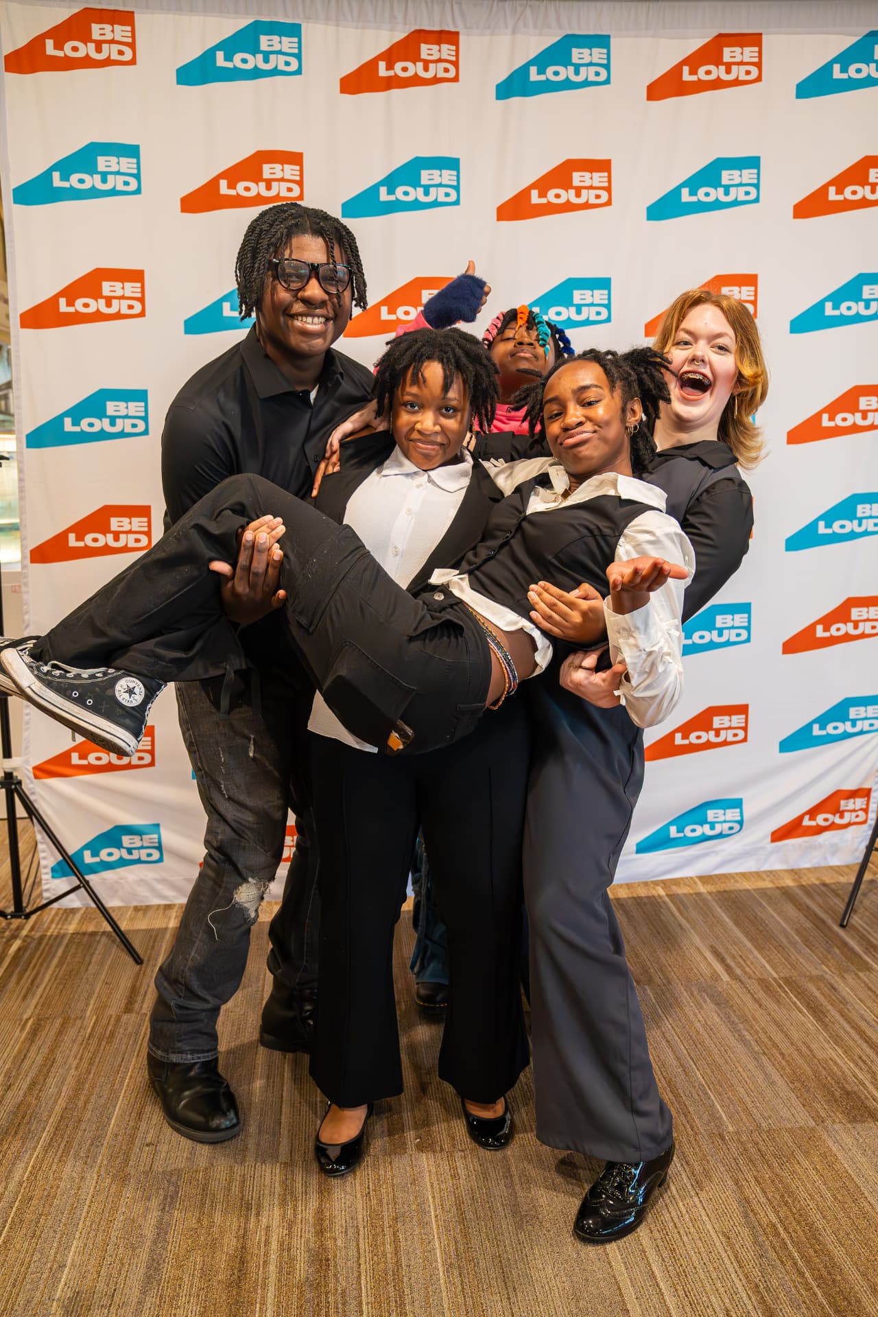 Be Loud students laughing together in front of a Be Loud step-and-repeat banner
