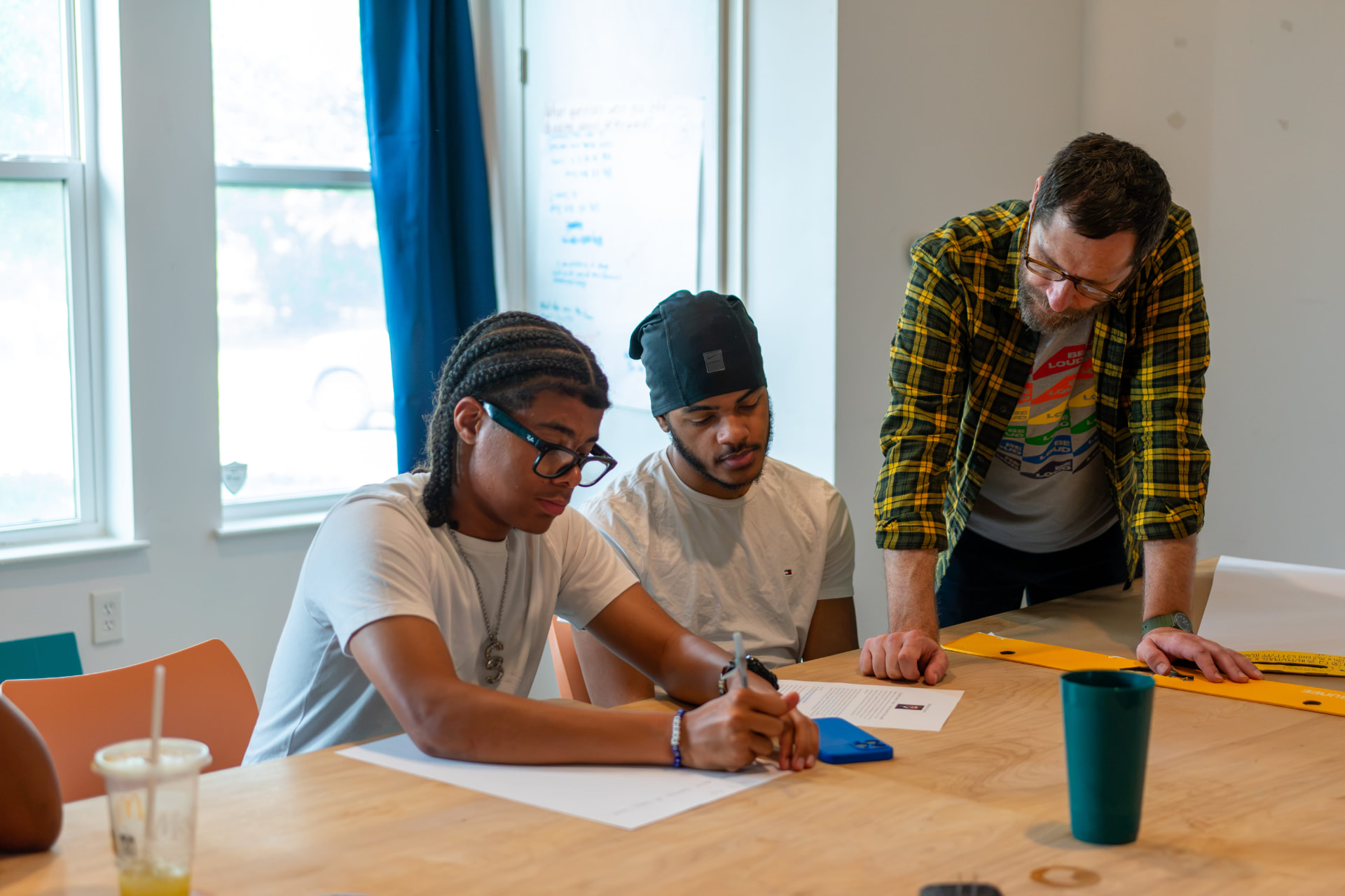 A Be Loud facilitator leaning in as two young people work through a lesson at a table