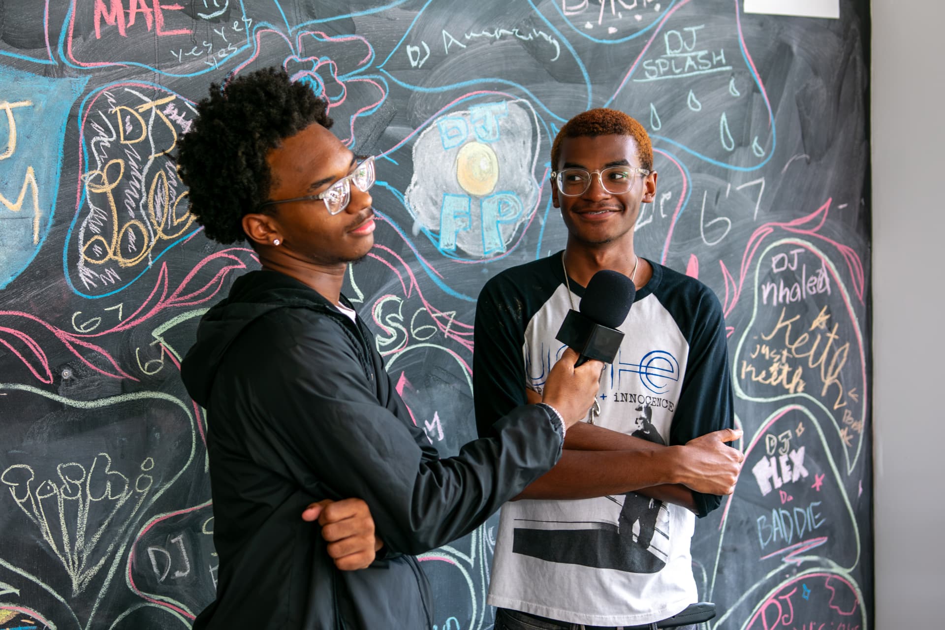 Two Be Loud youth producers interviewing each other in front of a chalkboard wall